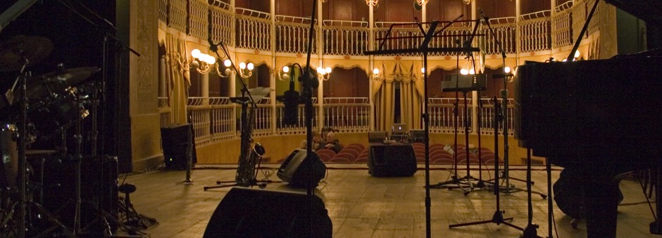 Un teatro visto dal palco. Si vedono inoltre un pianoforte, una batteria, due sassofoni, diversi microfoni e leggii. Il luogo ideale per la pratica e la didattica strumentale.